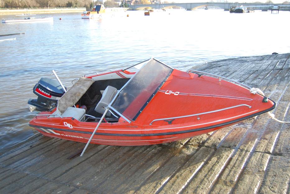 Red speedboat with a Yamaha engine on a boat ramp next to a body of water.
