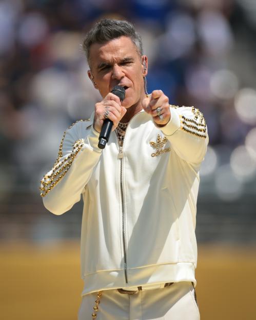 Robbie Williams singing while pointing at the audience.