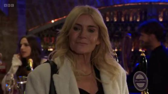 A blonde woman in a white coat at a bar.