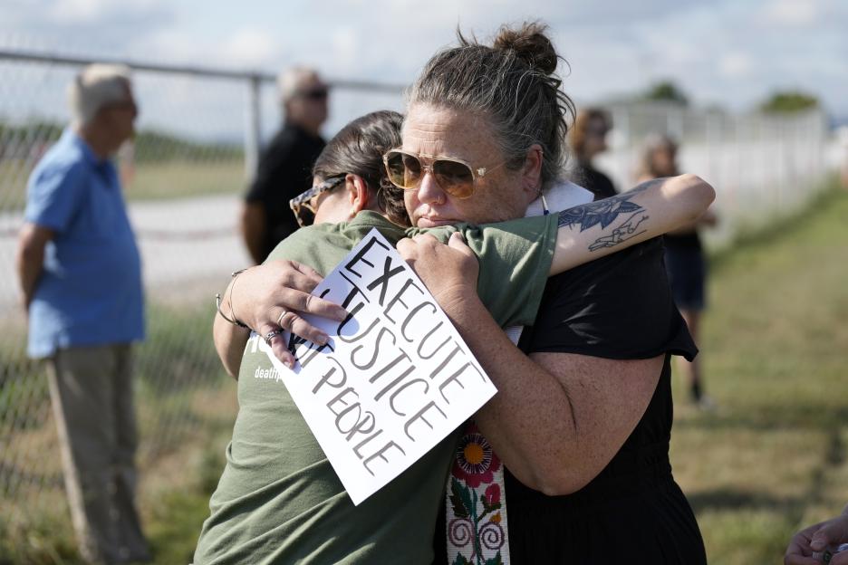 Two women embracing at an anti-death penalty protest, one holding a sign that reads "Execute Justice, Not People".