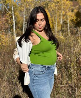 Woman in green top and jeans standing in autumnal setting.