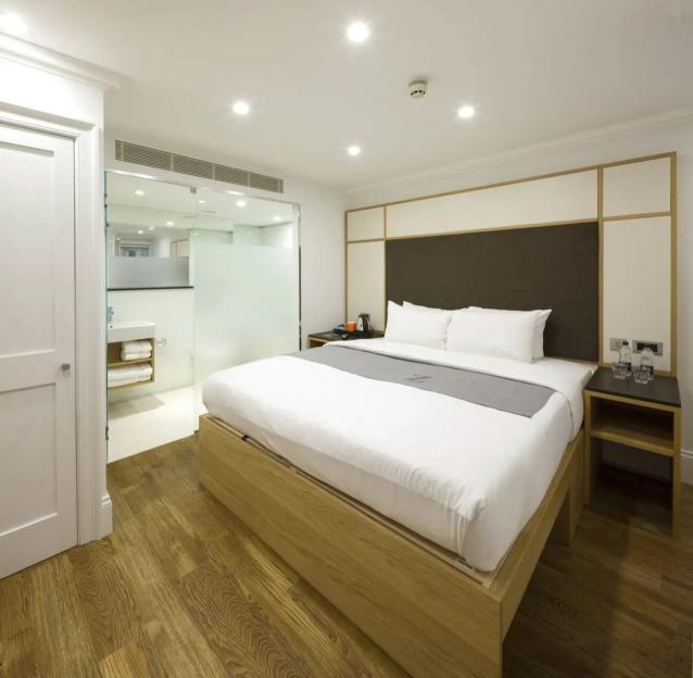 Hotel room with a bed, wood floors, and a bathroom with a glass door.