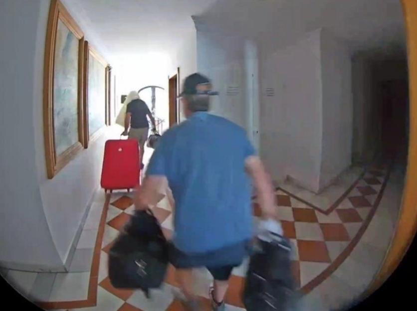 Security camera footage of two people carrying luggage down a hotel hallway.