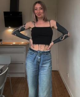 Woman with extensive arm tattoos wearing a black tank top and jeans.