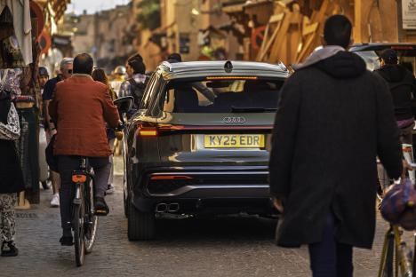 Rear view of a green Audi Q5 driving down a narrow street.