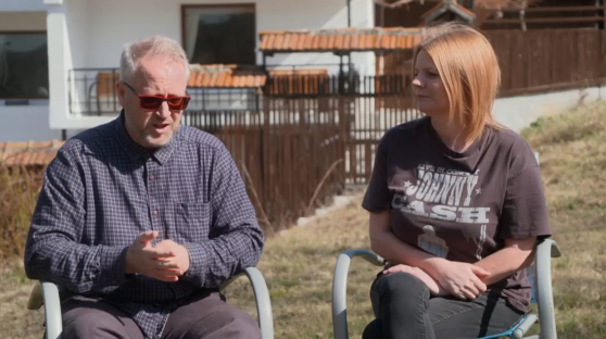 Two people sitting outdoors in chairs, talking.