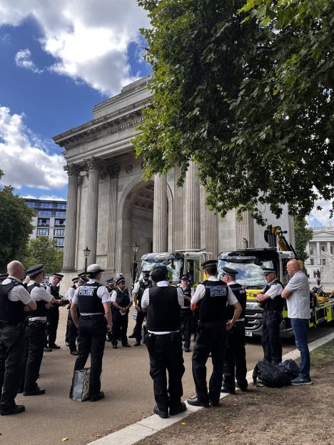 Police officers standing near a tow truck in front of an archway.