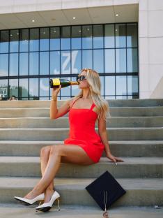 Woman in red dress celebrating graduation with champagne.
