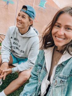 Two women sitting together, one wearing a grey hoodie that says 
