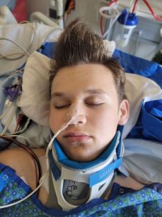 Teenage boy in hospital bed wearing a neck brace.