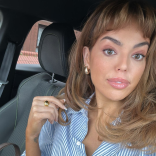 Woman in a car wearing gold jewelry and a blue striped shirt.