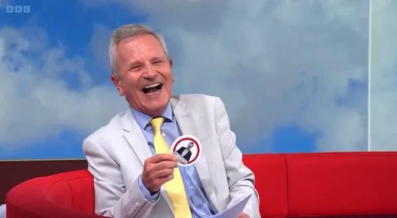 A laughing BBC presenter holding a sticker.