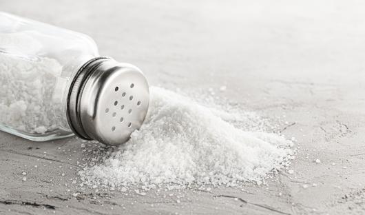 Spilled salt next to a salt shaker.