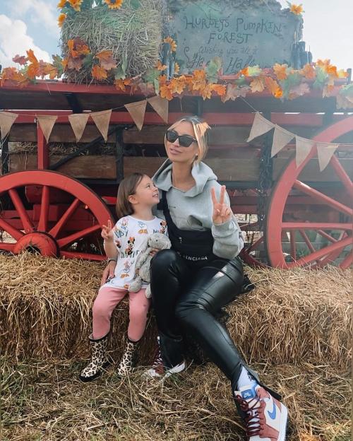 A woman and a young child giving peace signs while sitting on a hay bale at a pumpkin patch.