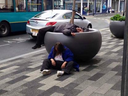 Two people sleeping in large planters at a bus station.