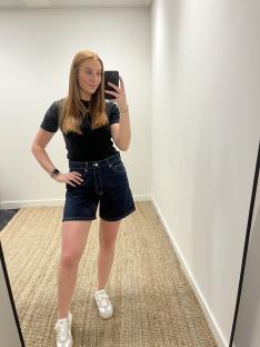 Woman in dark denim shorts and a black shirt taking a selfie.
