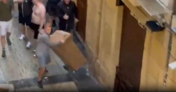 Person carrying a large box while being chased by a group of people.