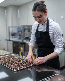 A pastry chef arranging chocolate eggs on a cooling rack.