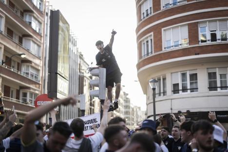 Tottenham Hotspur fan standing atop a traffic light, celebrating amidst a crowd of supporters.