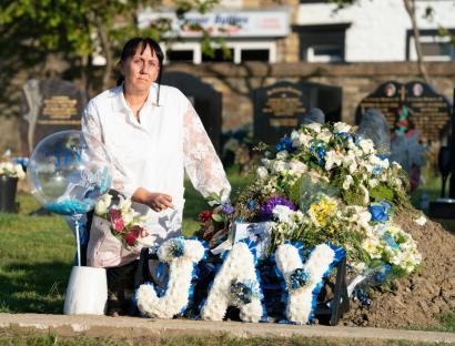 Woman mourning at a gravesite with floral tributes spelling