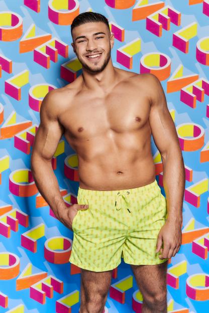 Tommy Fury posing in yellow swim shorts with a pineapple pattern.