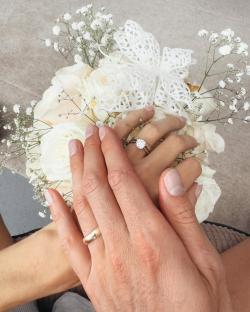 Two hands with wedding rings resting on a white rose bouquet.