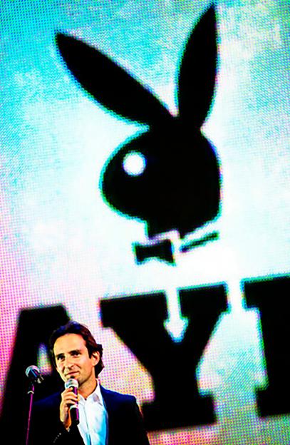 Vladimir Lyaporov speaking into a microphone in front of a large Playboy Bunny logo.