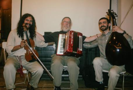 Three musicians playing violin, accordion, and oud.
