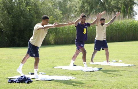 Three England soccer players stretching on mats outdoors.