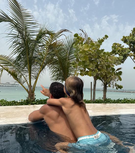 Man and child in a pool looking out at the ocean.