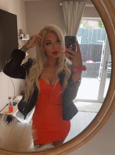Woman in orange dress taking a selfie in a mirror.