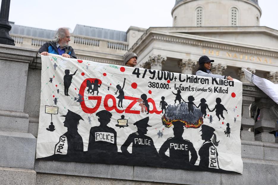 Protesters holding a banner stating "479,000+ Children Killed, 380,000+ Infants (under 5) Killed. Gaza is a nation of children! 70% of Gazans killed were children!" with silhouettes of children, police, and burning fires.