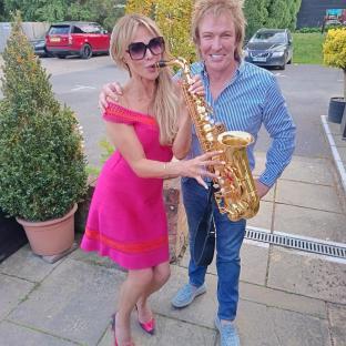 Woman in pink dress and man in blue shirt holding a saxophone.
