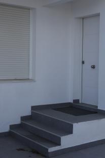 Exterior of a white building with a grey tiled stairway leading to a white door.