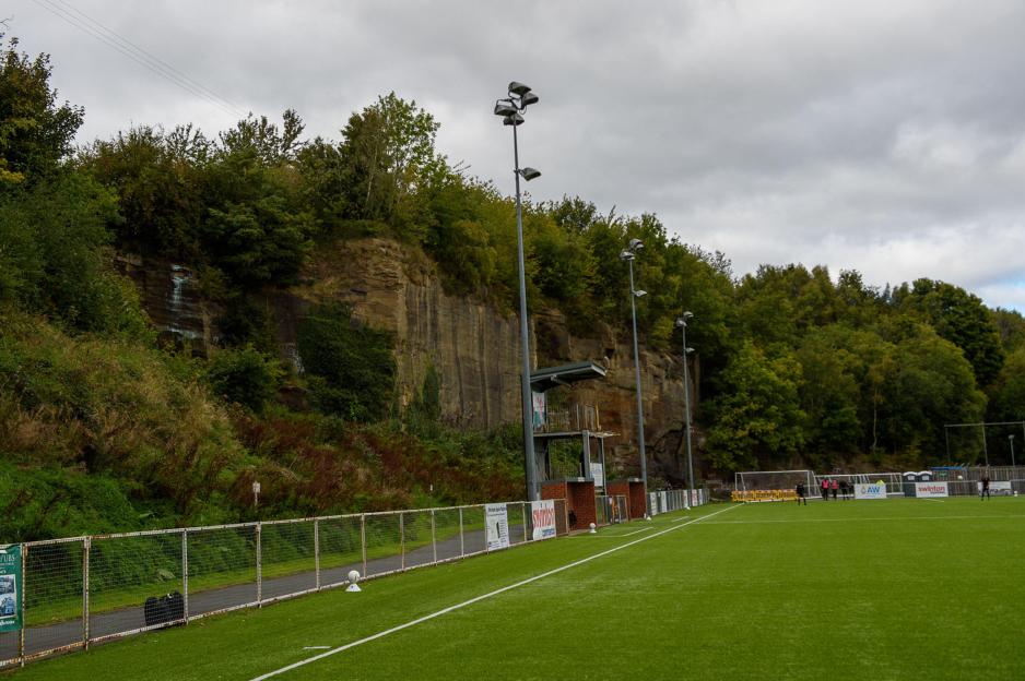 Soccer field with a rock face and trees in the background.