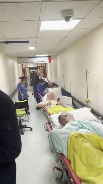 Hospital hallway with numerous patients on gurneys waiting for treatment.
