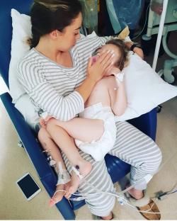 A mother comforting her young daughter in a hospital bed.
