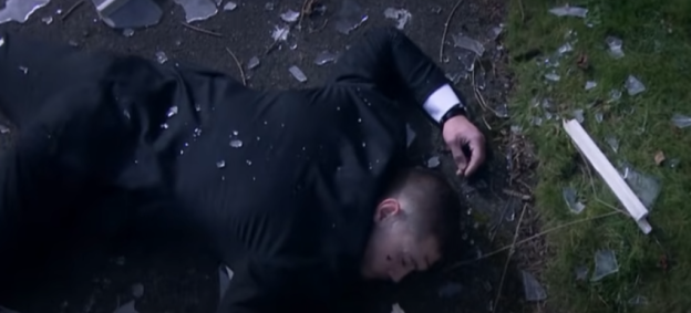 Man lying on the ground amidst broken glass.