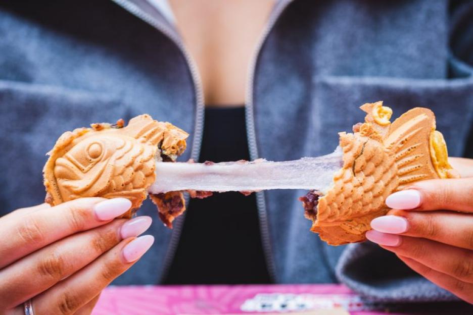 Hands pulling apart a taiyaki dessert, revealing a stringy white filling and red bean paste.