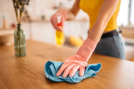Woman cleaning a wooden table with a spray bottle and cloth.