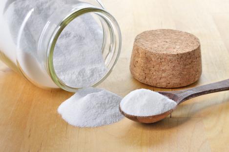 Baking soda in a glass jar and wooden spoon.