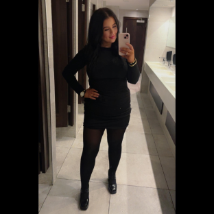 Woman in black dress taking a selfie in a restroom.