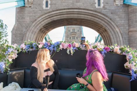 Two women on a London bar bus taking a photo of Tower Bridge.