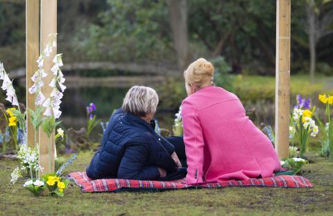 Two women sitting on a blanket outdoors, facing away from the camera.
