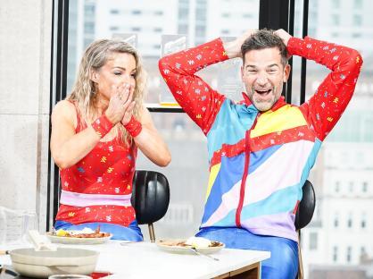 Photo of Helen Skelton and Gethin Jones in colorful athletic wear, reacting excitedly while sitting at a table with food.