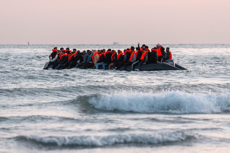 A group of migrants in orange life jackets on a dinghy in the English Channel.