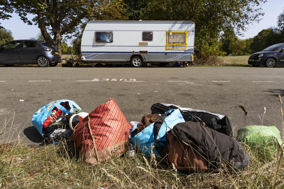 A caravan parked on the roadside with bags of belongings on the verge.