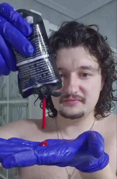 A person wearing blue gloves pours red hair dye from a tube into their gloved hand.