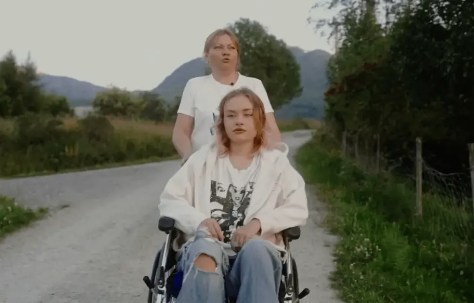 Woman pushing a young woman in a wheelchair down a country road.