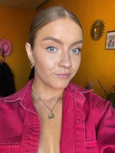 Woman wearing a pink shirt and gold jewelry.